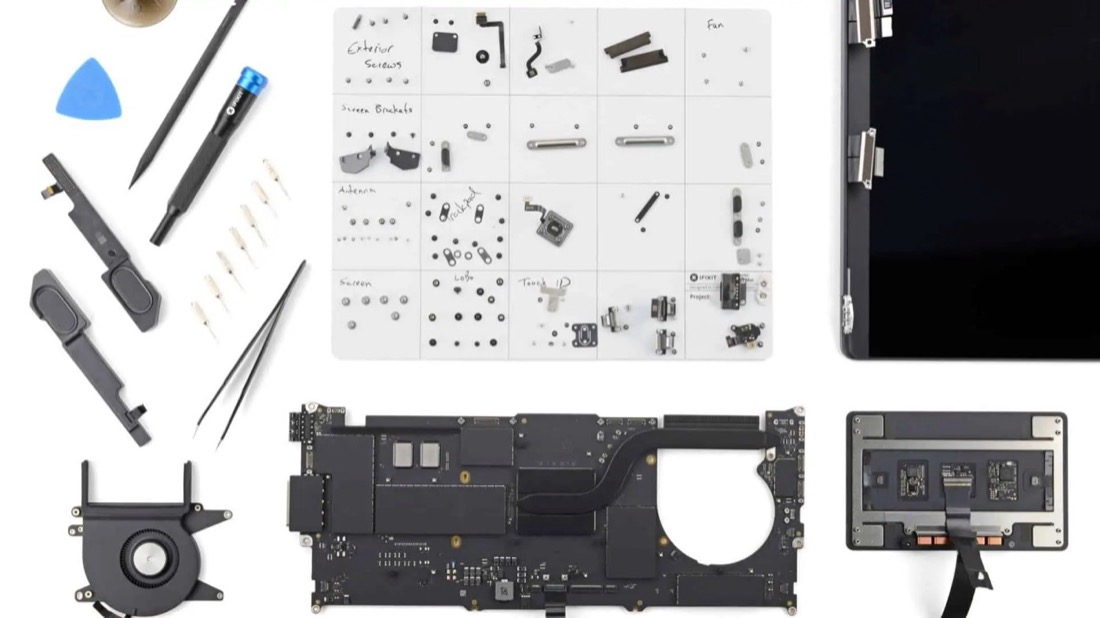 Placa, ventilador, trackpad y pantalla de una MacBook desarmada sobre la mesa de trabajo